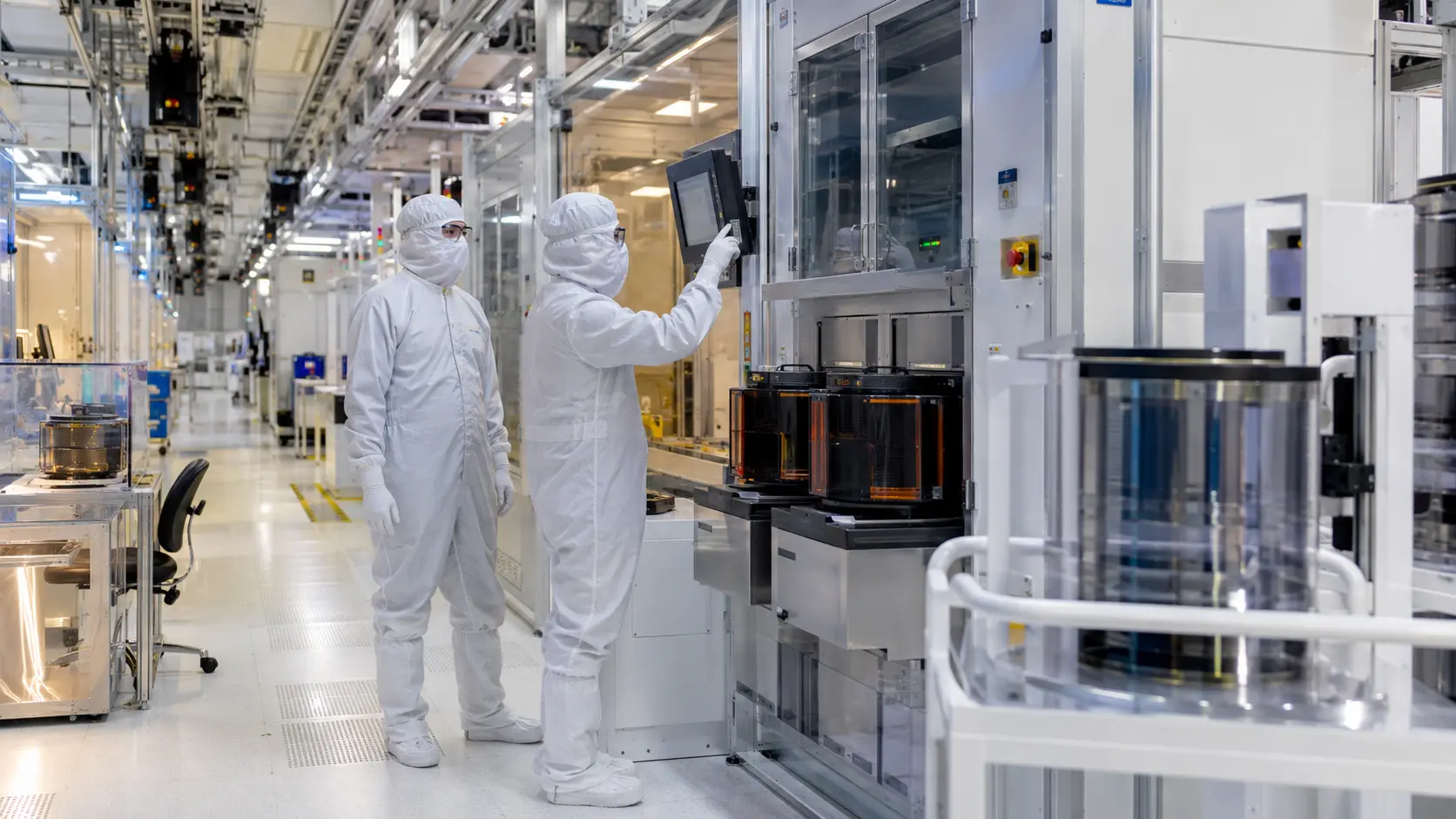 Semiconductor engineers operating wafer-processing equipment inside a modern fabrication cleanroom